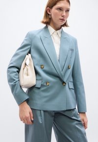 Φωτεινό γαλάζιο διπλό σακάκι με μεγάλα καφέ κουμπιά, συνδυασμένο με ταιριαστό παντελόνι και μια μικρή κρεμ τσάντα. Λεπτή υφή.