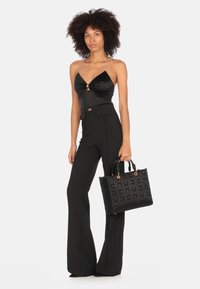 Body in satin nero con scollatura profonda e dettaglio annodato, abbinato a pantaloni neri a vita alta e a campana e una borsa nera strutturata.