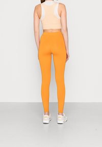 Oranga leggings i stretchmaterial, med hög midja och åtsittande silhuett, i kombination med en beige kort topp och vita sneakers.