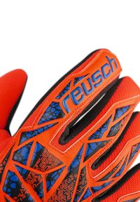 Guanto da portiere rosso con un design testurizzato nero e blu, caratterizzato da un prominente logo "Reusch" e dettagli protettivi per le dita.