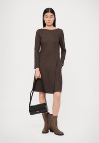 Brown textured dress with long sleeves and pockets, paired with brown heeled boots and a small black handbag with a crocodile pattern.