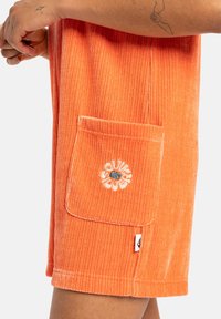 Oranje corduroy shorts met een voorzak met geborduurd bloemenontwerp, zichtbare textuur en een klein zijlabel.