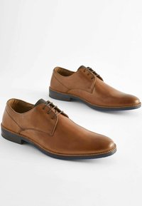 Zapatos de vestir de cuero marrón con un acabado suave, puntera redonda, diseño con cordones y una suela oscura en contraste. Detalle de costura minimalista.