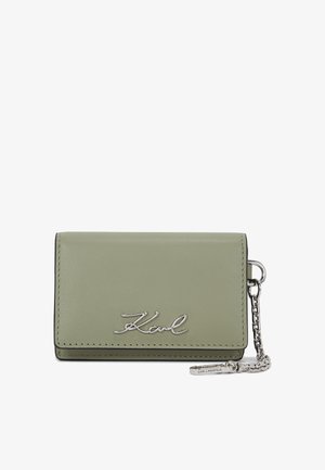 Tarjetero de cuero verde con el logo plateado "Karl", accesorio de cadena y ribete negro contrastante. Diseño compacto y rectangular.