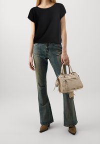 Top nero a maniche corte, jeans blue dal taglio svasato, borsa beige con zip e décolleté beige a punta. La texture del denim logoro è visibile.