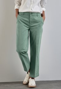 Pantalons verts à coupe décontractée en coton doux, dotés d'une fermeture à bouton, de poches latérales et d'un design à jambes droites. Accentué par des coutures minimales.