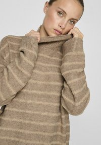 Bežna pletena jopica z visokim ovratnikom, ki ima vertikalne proge v svetlejši barvi, rebraste manšete in mehak tekstur.
