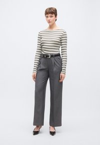 Ριγέ μακρυμάνικο τοπ σε ανοιχτό και σκούρο γκρι, σε συνδυασμό με ψηλόμεσα παντελόνια σε σκούρο γκρι και μαύρα παπούτσια με μυτερή μύτη.