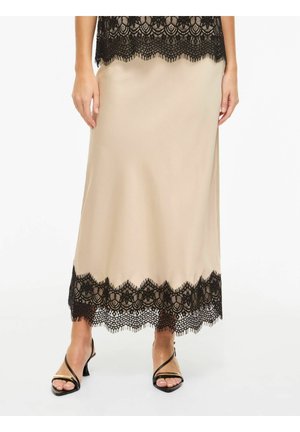 Jupe en satin beige avec un bord en dentelle florale noire à l'ourlet, portée avec des sandales noires à talons et à brides, montrée de la taille aux pieds.