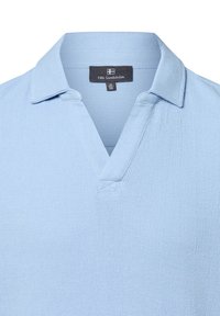 Himmelblaues Poloshirt aus strukturiertem Stoff. Mit V-Ausschnitt, kurzen Ärmeln und einem Etikett mit Marken- und Größeninformationen.