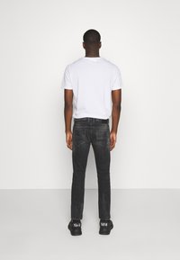 Černé džíny z denimu s úzkým střihem, designem s pěti kapsami a kontrastním prošitím. Noseny s bílým tričkem s krátkým rukávem a černými teniskami.