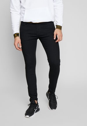 Zwarte skinny jeans van denim met een gladde textuur, voorzien van een mid-rise pasvorm en subtiele stikdetails. Gepaard met zwarte sportieve schoenen.