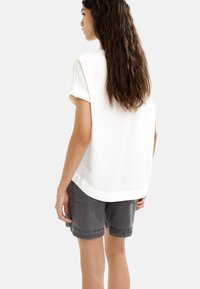 Jasny, krótki rękaw, luźny T-shirt w połączeniu z szarymi szortami. Tkanina wydaje się gładka o delikatnym połysku.