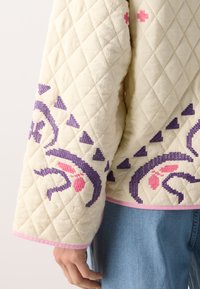 Quiltet kremjakke med lilla og rosa broderimønstre, med pink kant og teksturert stoff. Avslappet passform og vide ermer.