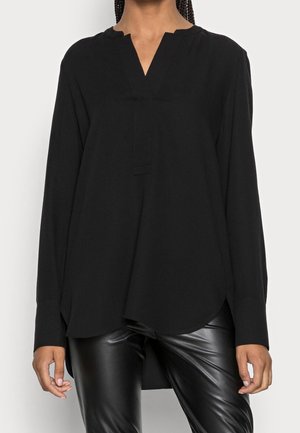 Maglietta nera a maniche lunghe con scollo a V, caratterizzata da una sottile texture e orlo arrotondato, abbinata a pantaloni neri in ecopelle.