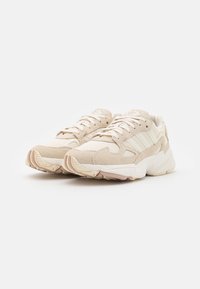 Ljusbeiga sneakers i mocka och nätmaterial, med tre ränder på sidan, robust sula och texturerad detaljering på ovandelen.