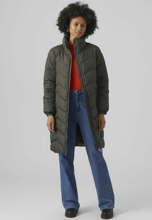 Un long manteau rembourré vert olive avec un col haut ; doté d'une fermeture éclair sur le devant et d'un motif matelassé en losanges. Assorti à un jean bleu à jambes larges.