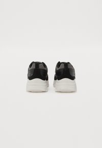 Schwarze und graue Sportschuhe mit einem strukturierten Mesh-Obermaterial, glatten schwarzen Akzenten und einer weißen gepolsterten Sohle, von hinten betrachtet.