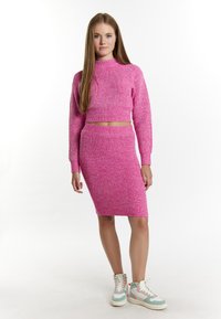 Top corto a maniche lunghe in maglia a coste rosa abbinato a una gonna lunga fino al ginocchio. Presenta una silhouette aderente e una texture soffice.