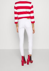 Top de rayas rojas y blancas con mangas 3/4, combinado con jeans ajustados blancos y botines de tacón bloque rojo con detalles en negro.