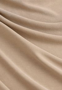 Tissu tricoté beige avec une texture lisse et un léger éclat, présentant des motifs en côtes diagonales et un drapé doux.
