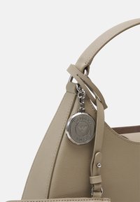 Beżowa skórzana torebka o gładkiej fakturze, z zakrzywionym uchwytem, odpinanym srebrnym charmsiem oraz subtelnym kontrastem wnętrza.