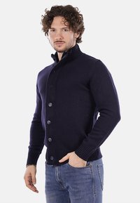 Cardigan lavorato a maglia blu navy con colletto alto, chiusura con bottoni e polsini a coste. Presenta un tessuto testurizzato, un design aderente e bottoni a contrasto.