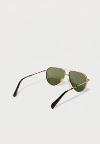 Óculos de sol aviador em metal dourado com lentes verdes e hastes em padrão tartaruga preta. Armações finas com um design minimalista.