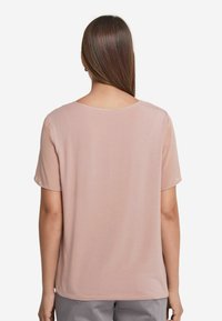 Ljusrosa kortärmad blus med rund halsringning och slät textur. Baksidan är enkel, med en avslappnad passform och utan synlig hårdvara.