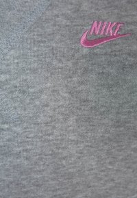 Šedá textilie s hladkým povrchem a viditelným švem. Na dolní pravé straně se nachází růžové vyšívané logo Nike.