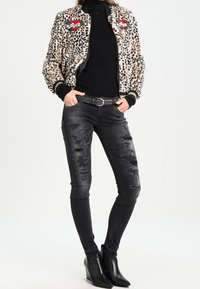 Veste bomber à imprimé léopard avec patchs brodés, col roulé noir, jean skinny noir déchiré et bottines noires.