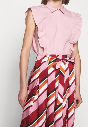 Ærmeløs lyserød bluse med flæseærmer, kombineret med et højtaljet, plisseret skørt med diagonale striber i rød, lyserød, orange, hvid og sort.