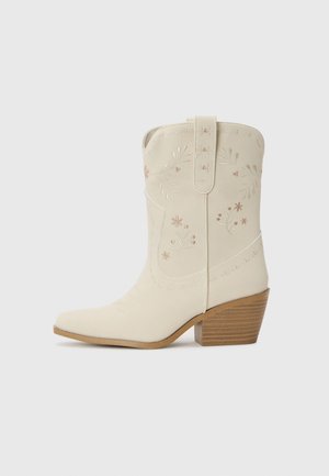 Botă de cowboy din piele albă cu broderie florală, vârf ascuțit și toc din lemn stratificat. Prezintă cusături decorative pe tijă.