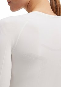 Biała koszulka sportowa z teksturowanym wzorem i bezszwowym designem, z widocznymi szwami i żebrowanymi akcentami wzdłuż ramion.