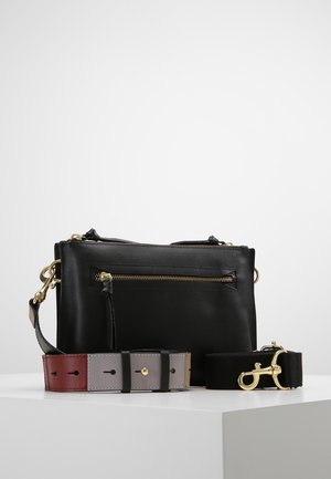 Musta nahkainen olkalaukku, jossa etutasku vetoketjulla, kullanväriset metalliosat ja kaksi irrotettavaa olkahihnaa—yksi moniväristä nahkaa, toinen mustaa kangasta kultaisella lukolla.