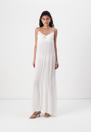 Long, white, sleeveless dress made of lightweight fabric. It features a V-neckline and a flowy silhouette, complemented by minimalistic strappy sandals.