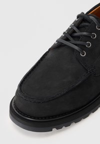 Črne semiš čevlje z vezalkami, ki imajo zaobljen nos in teksturirano površino. Guma podplat z robustnim vzorcem, šivana ob robovih.