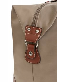 Sac en tissu beige avec un accent en cuir brun, présentant une fermeture à pression en métal argenté, des détails de couture et un dessus zippé.