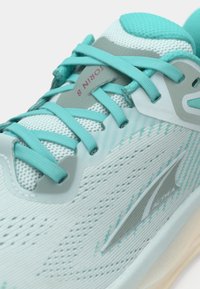 Light teal athletic shoe featuring a textured mesh upper, contrasting laces, and a cushioned sole with a subtle logo detail.