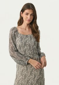 Rochie lungă cu mâneci lungi, cu un model floral, guler pătrat, mâneci plisate, material moale și o paletă de culori deschise, în crem și negru.