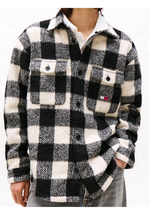 Zwart-wit geruit wollen jack met knoopsluitingen op de borstzakken, gedragen over een wit hemd met kraag en gecombineerd met grijze spijkerbroeken.