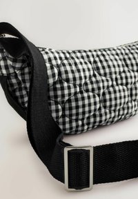 Gestepptes schwarz-weißes Gingham-Tasche mit einem dicken schwarzen Riemen und einer silbernen rechteckigen Schnalle, mit einer runden Form und strukturierter Oberfläche.