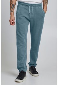 Blå sweatpants med elastisk talje, snører og sidelommer. Ribbenede manchetter ved anklerne og et blødt, tekstureret stof.