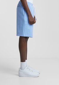 Shorts en coton bleu clair avec une taille élastique, cordon de serrage, poches latérales, et des baskets blanches avec des détails texturés.