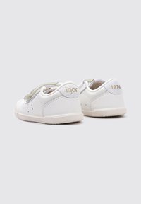 Zapatos de cuero blanco con correas gris claro, que presentan acentos dorados "igor" y "1974" en la parte posterior. Material suave y texturizado, punta redondeada.