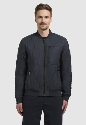 Schwarze gesteppte Jacke mit hexagonalem Muster, Frontreißverschluss, gerippte Bündchen und Saum. Verfügt über eine Brusttasche und Seitentaschen. Lockere Passform.
