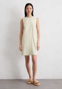Hellgrünes ärmelloses Kleid mit Rundhalsausschnitt, geradem Schnitt und sichtbaren Nahtdetails. Kombiniert mit beigen, geflochtenen Plateausandalen.