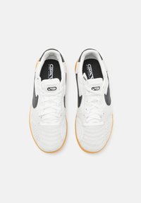 Un par de zapatillas Nike blancas con el swoosh negro, cordones blancos y suelas de goma naranja, mostradas desde arriba sobre un fondo blanco.