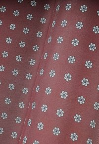 Bordowy materiał z powtarzającym się wzorem małych białych kwiatów. Tekstura jest gładka i lekka, idealna na odzież lub akcesoria.