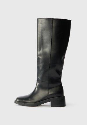 Fekete, térd fölé érő bőr csizma alacsony blokk sarkával és sima felületével, oldalról látható egyszínű világos háttér előtt.